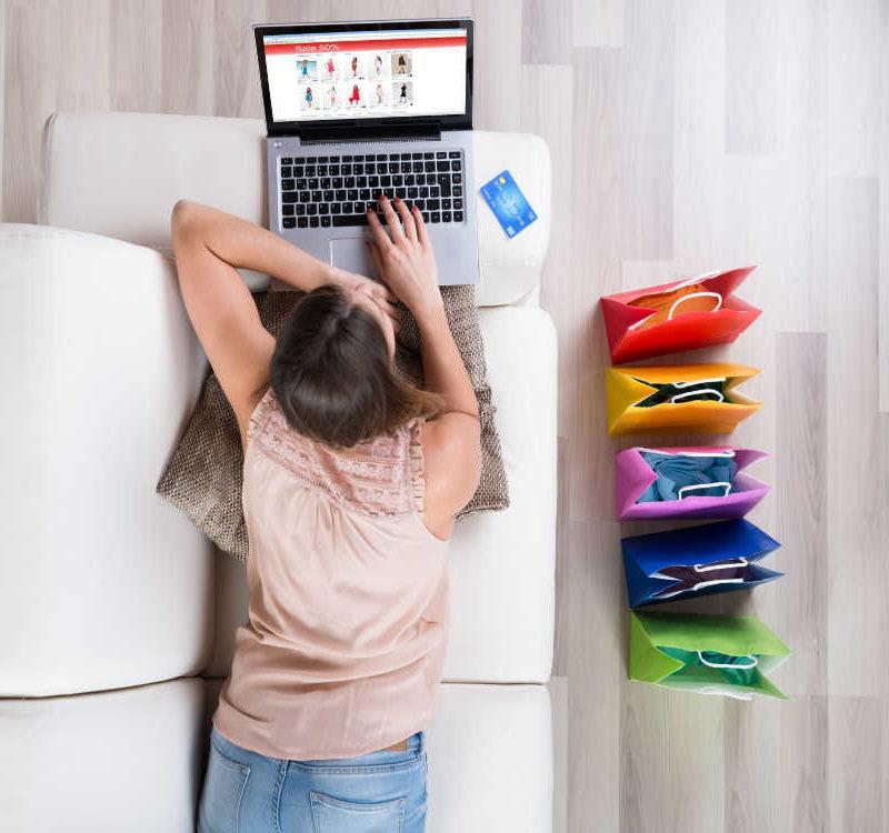 Young Woman On Sofa Shopping Online With Laptop
